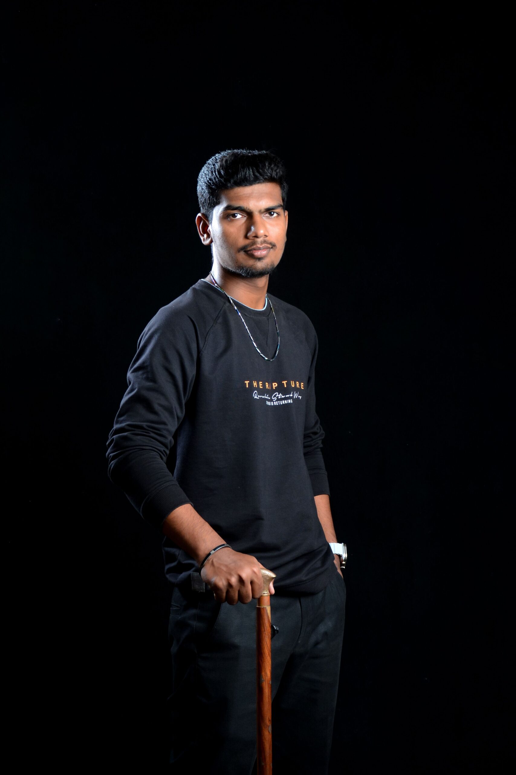 pexels photo 18166948 18166948 Portrait of a young man standing confidently with a walking stick against a black background.